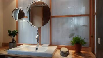 A bathroom with a white sink, a round mirror, and a wooden-framed window.