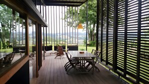 A covered outdoor area with a wooden deck, a table, chairs, and a view of the landscape. - Gîte Dilos – Holiday Home in Gan (Gan)