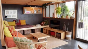 A cozy living space with a sofa, TV, and shelves with plants. - Gîte Dilos – Holiday Home in Gan (Gan)