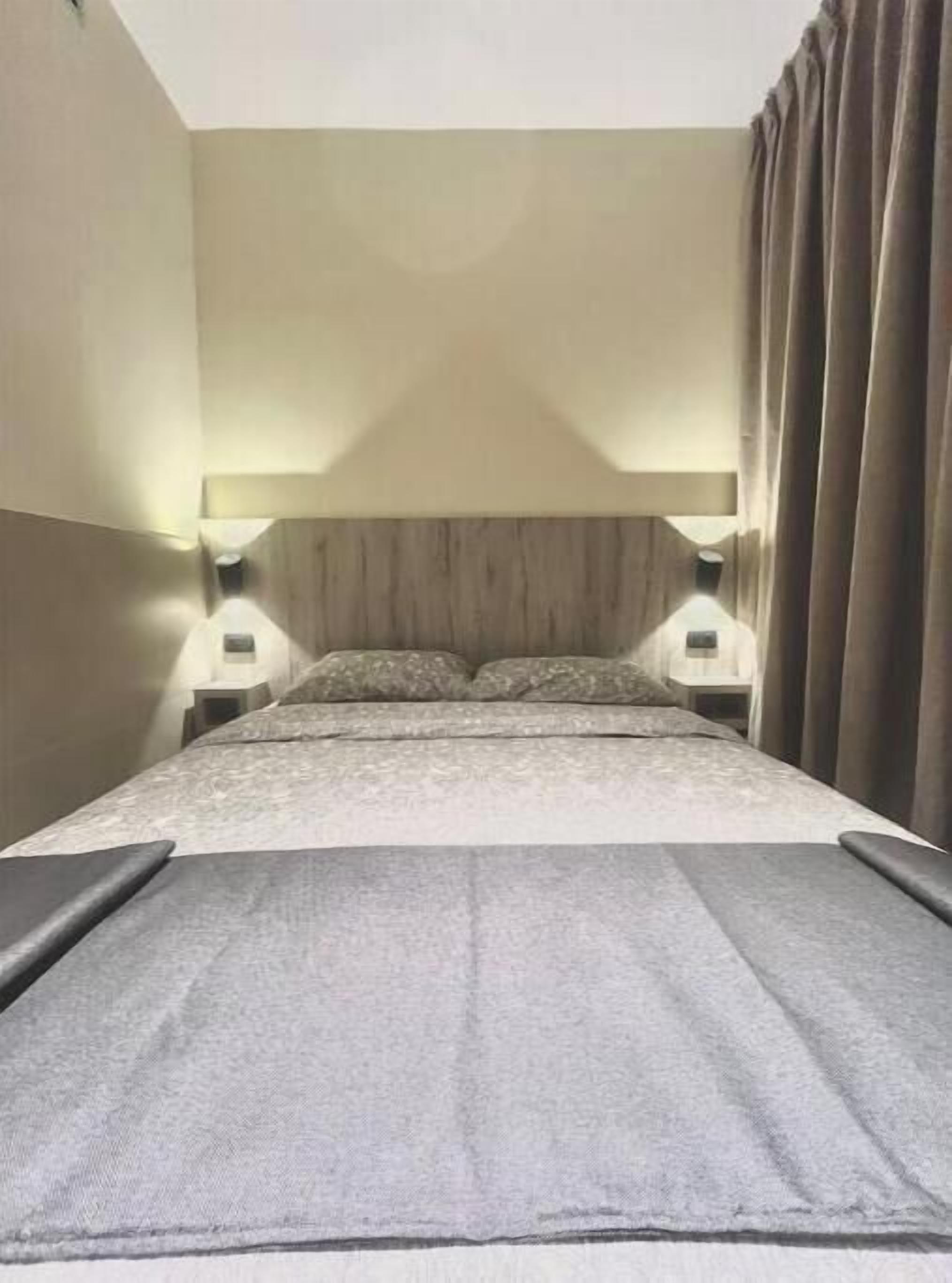 A hotel room with a large bed, two bedside tables, a headboard, and a curtain.