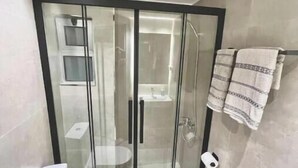 A modern bathroom with a glass-enclosed shower, a toilet, and a towel rack.