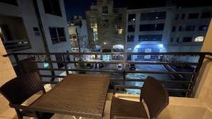 A balcony with a table and two chairs, overlooking a cityscape at night.