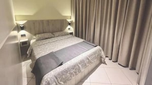 A hotel room with a large bed, two bedside tables, and a curtain.