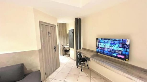 A modern living room with a flat-screen TV mounted on the wall, a grey sofa, and a tiled floor.