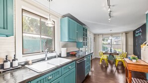A kitchen with teal cabinets, a white sink, and a wooden dining table with yellow chairs.