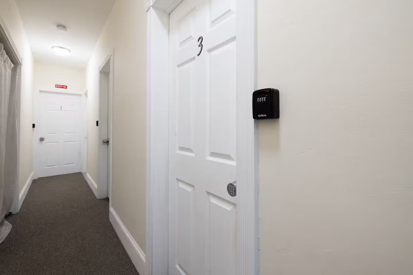 A hallway with white doors, one marked with the number 3, and a doorbell on the wall.