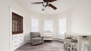 A room with a ceiling fan, a gray armchair, a white desk with two chairs, and a window with blinds. - Spacious Urban Townhouse • Groups and Family (Hartford)