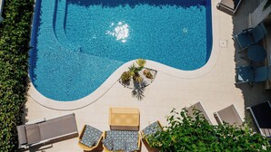 An aerial view of a rectangular swimming pool with a small island in the center, surrounded by lounge chairs and a small garden area. - Captain's Villa (Budva)