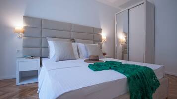 Una cama bien tendida con un cubrelecho de encaje verde, una lámpara de noche y un sombrero en la mesita de noche.