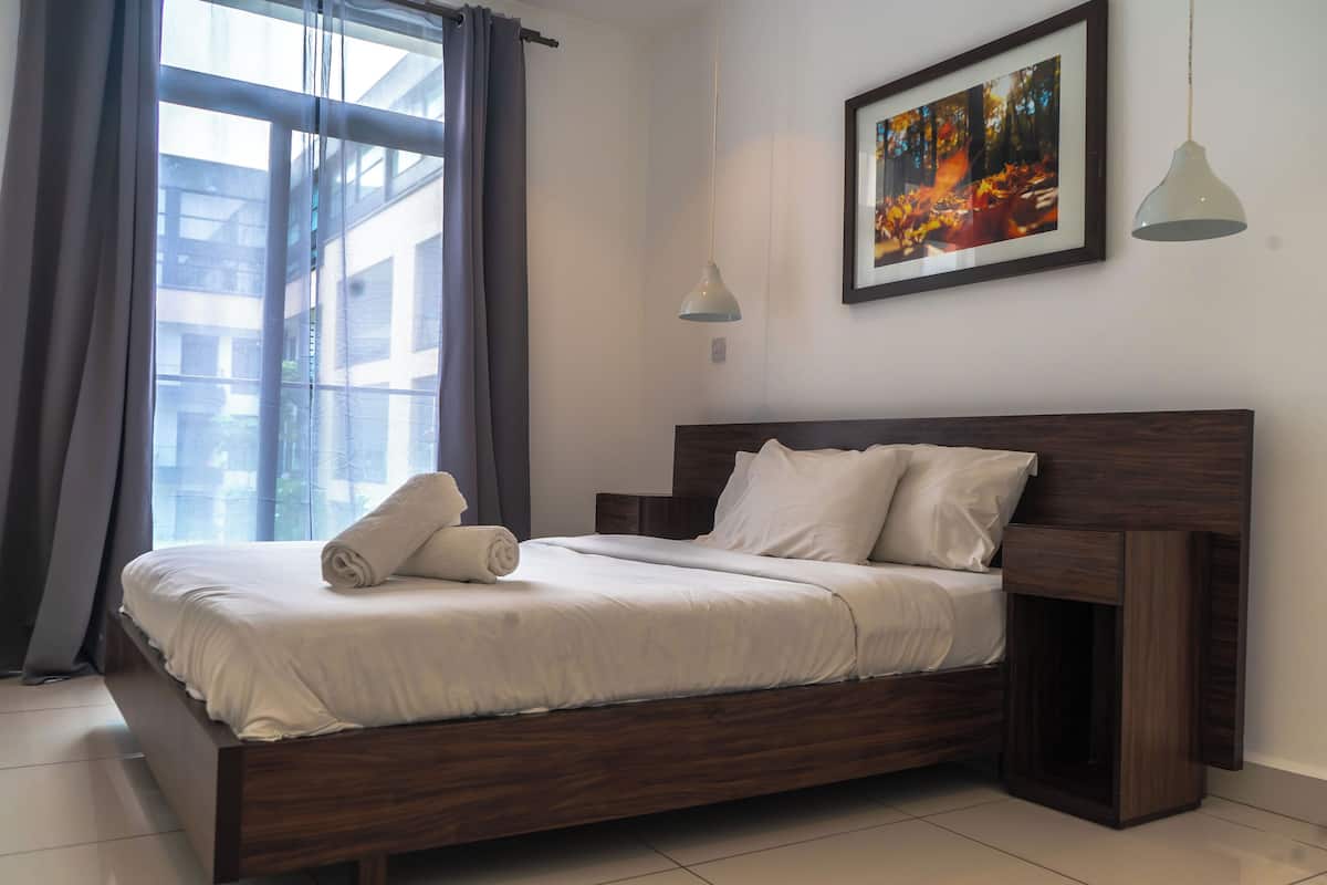 A neatly made bed with a wooden headboard, a framed picture on the wall, and a window with curtains.