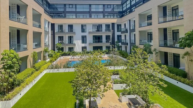 A modern building with multiple balconies, a central courtyard with a pool, and surrounding greenery. - RoyalRest at Embassy Gardens (Accra)