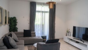 A modern living room with a sofa, armchair, and a TV on a white stand. - RoyalRest at Embassy Gardens (Accra)