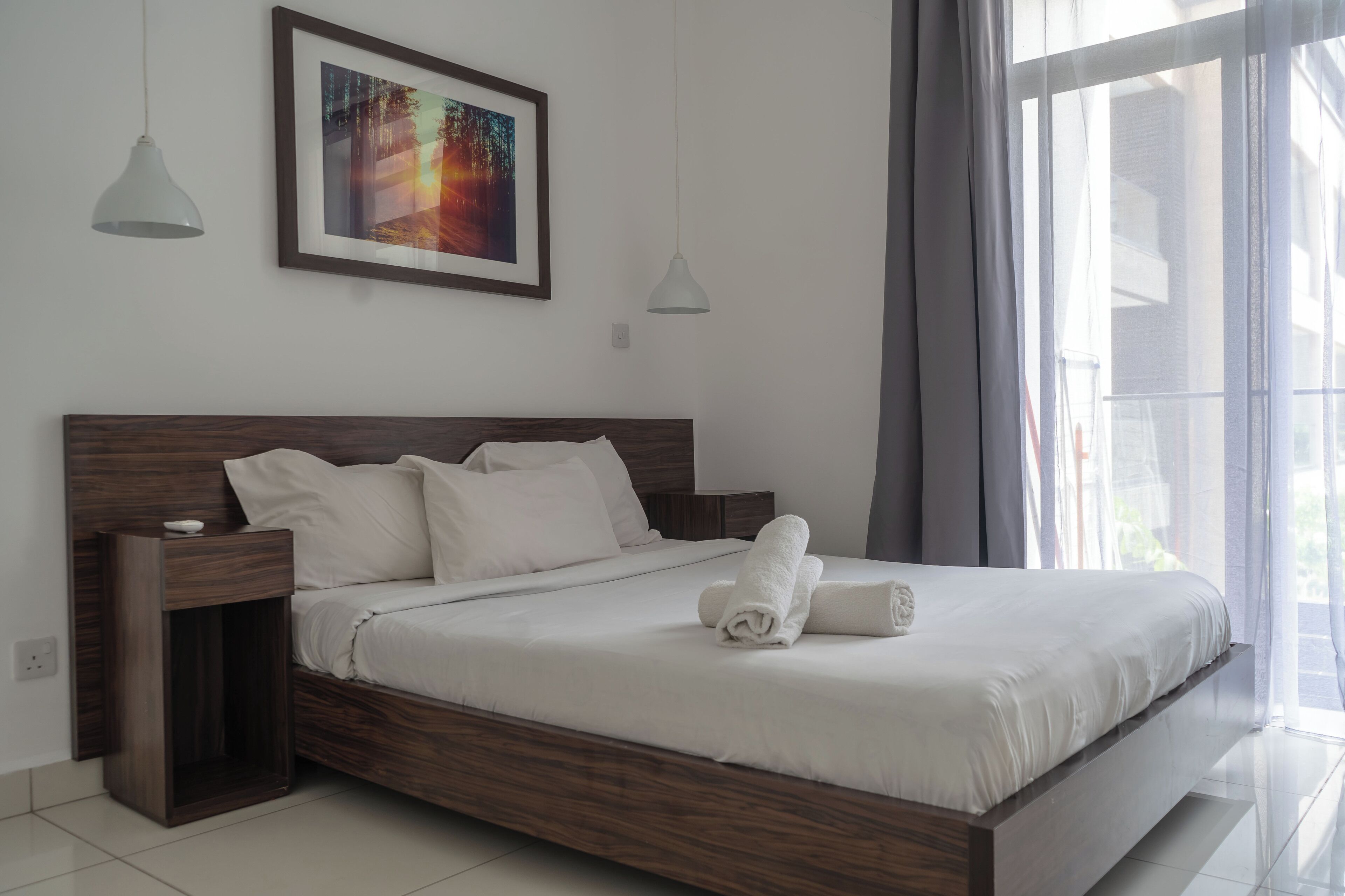 A modern bedroom with a wooden bed frame, white bedding, and a framed picture on the wall.