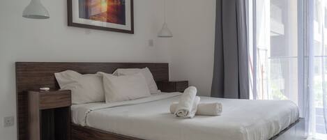 A modern bedroom with a wooden bed frame, white bedding, and a framed picture on the wall.