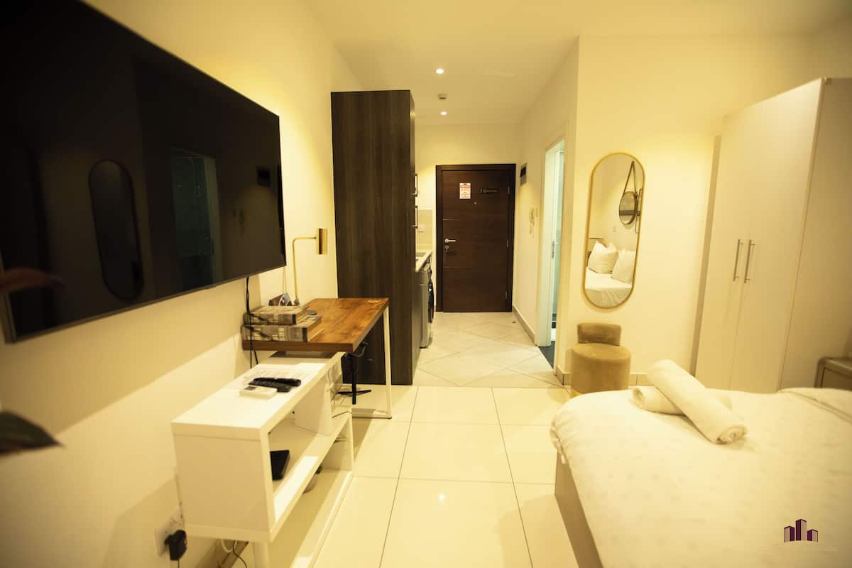 A hotel room with a bed, a desk, a mirror, a wardrobe, and a bathroom visible through an open door.