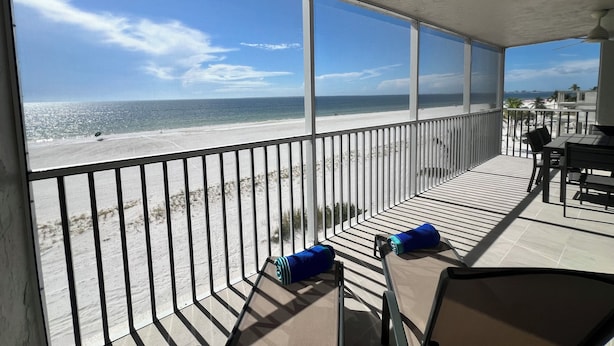 Un balcón con vista a la playa, una mesa y dos sillas.