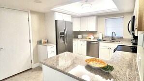 Una cocina moderna con armarios blancos, encimera de granito, refrigerador de acero inoxidable y tragaluz sobre el fregadero.