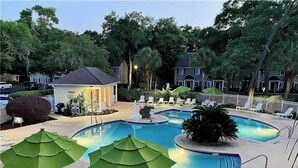Une piscine entourée d’arbres et d’un petit bâtiment, avec des chaises longues et des parasols à proximité.
