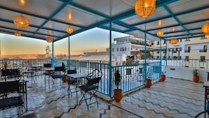 An outdoor terrace with a view of the cityscape, featuring a patterned floor, blue railings, and hanging wicker lamps. - Dar Fes Flores  (Fes)