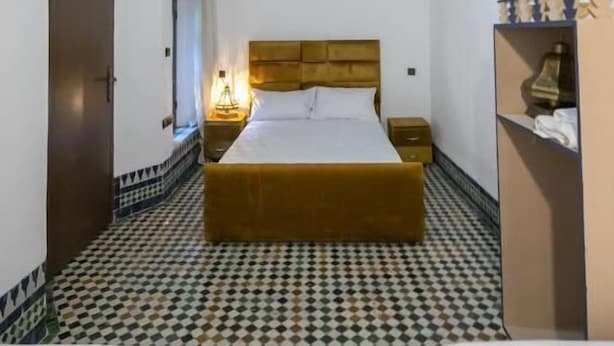 A room with a checkered floor, a bed with a wooden headboard, a wardrobe, and a hanging light fixture. - Dar Fes Flores  (Fes)