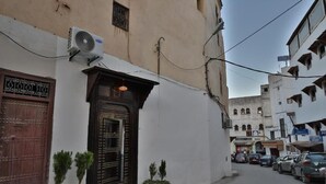 A narrow street with a building featuring a traditional wooden door and a small air conditioning unit mounted on the wall. - Dar Fes Flores  (Fes)