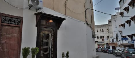 A narrow street with a building featuring a traditional wooden door and a small air conditioning unit mounted on the wall.