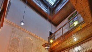 A high-ceilinged room with intricate wall designs, a patterned rug, and a sofa with patterned cushions. - Dar Fes Flores  (Fes)