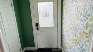 Un pasillo con una puerta blanca, un felpudo negro y una pared con un diseño de hojas.