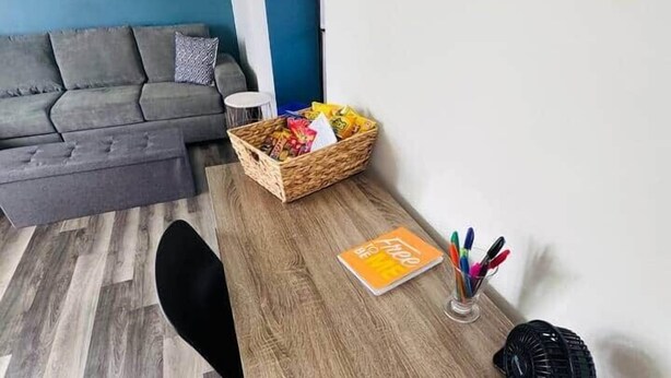 Une pièce avec un bureau en bois, une télécommande, un carnet et un panier rempli d’en-cas.