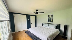 Un dormitorio con cama, un banco, un ventilador de techo y un cuadro en la pared.
