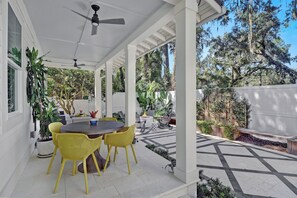 Une terrasse couverte avec une table et des chaises, entourée de plantes en pot et offrant une vue sur les arbres.