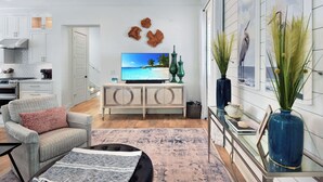 A modern living room with a flat-screen TV, a sofa, a coffee table, and a dining area with a glass table and chairs. - 3 bedroom/3.5 bath house.  Master on the main!  South end. (Saint Simons Island)
