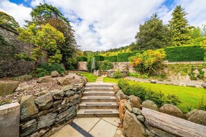 A stone staircase leading to a garden with a stone wall on one side and a wooden fence on the other.