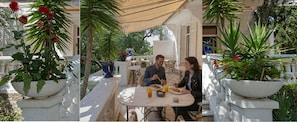 A dining area with a table and chairs, surrounded by potted plants and a covered patio.