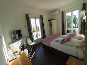 A hotel room with a bed, a desk with a chair, a TV, and a wardrobe.