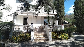 A white building with a covered porch, stone steps, and yellow flowers.