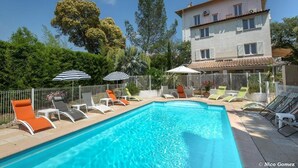 A swimming pool with lounge chairs and umbrellas, surrounded by a fence and trees. - Hôtel Le Thimothée (Saint-Raphaël)