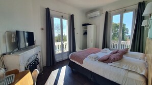 A hotel room with a bed, a TV, a desk, and a balcony with curtains. - Hôtel Le Thimothée (Saint-Raphaël)