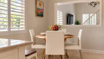 A dining area with a round table, white chairs, and a vase of flowers.