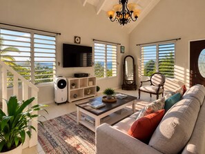 A spacious living room with a large sofa, a coffee table, a TV, and a staircase leading to a balcony with a view. - Bay View Island Escape 3BR + Generator + A/C (St. Thomas)