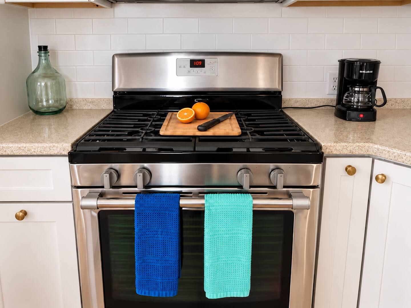 A kitchen with a stainless steel stove, a coffee maker, and a cutting board with an orange and a knife.