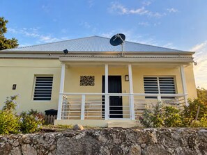 A two-story house with a satellite dish, a balcony, and a stone wall in the foreground. - Bay View Island Escape 3BR + Generator + A/C (St. Thomas)