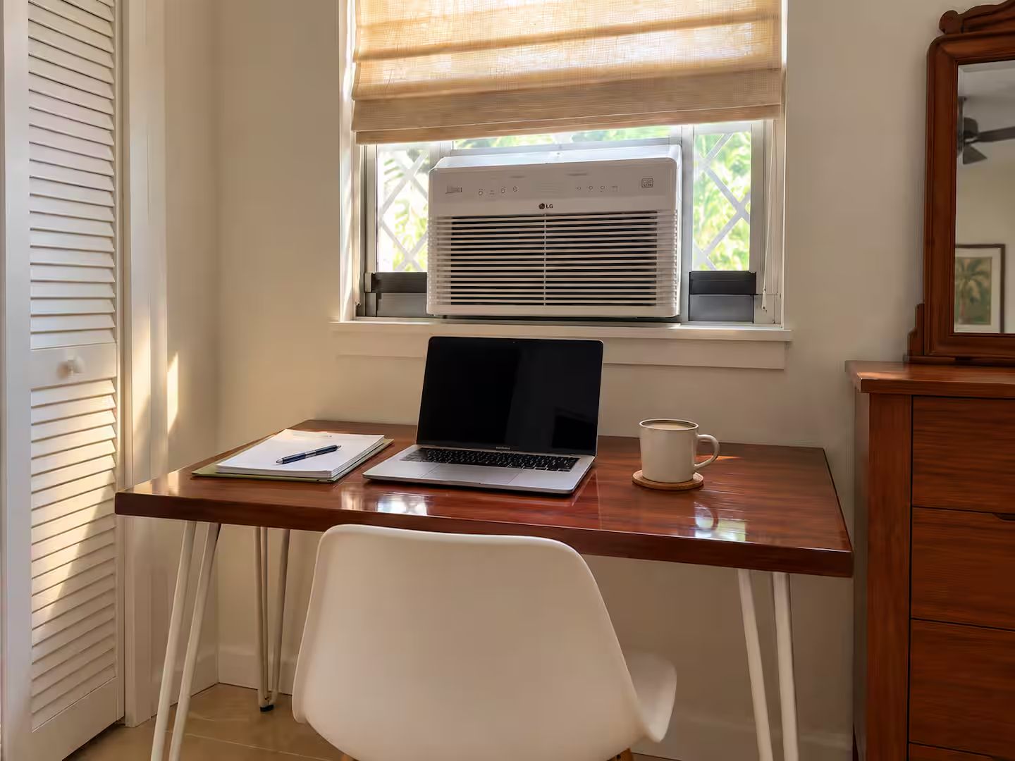 A workspace with a laptop, a notebook, and a cup on a wooden desk.