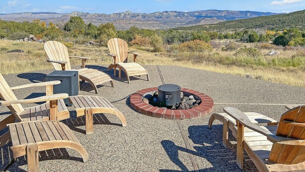 A patio with Adirondack chairs and a fire pit, overlooking a mountainous landscape.