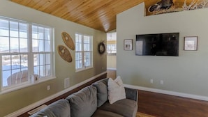 A living room with a wooden ceiling, a gray sofa, a flat-screen TV, and a large window.