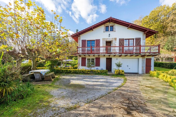 A two-story house with a balcony, a gravel driveway, and a well-maintained garden.