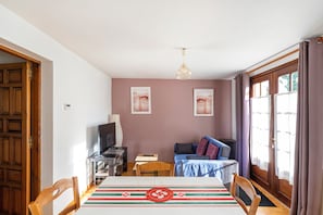 A dining area with a table, chairs, a television, and a sofa.
