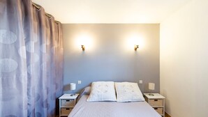 Een slaapkamer met een bed, twee nachtkastjes, een lamp, een gordijn en wandlampen.