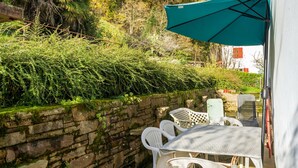 Een terras met witte kunststof stoelen en een tafel, een stenen muur en een groene parasol.