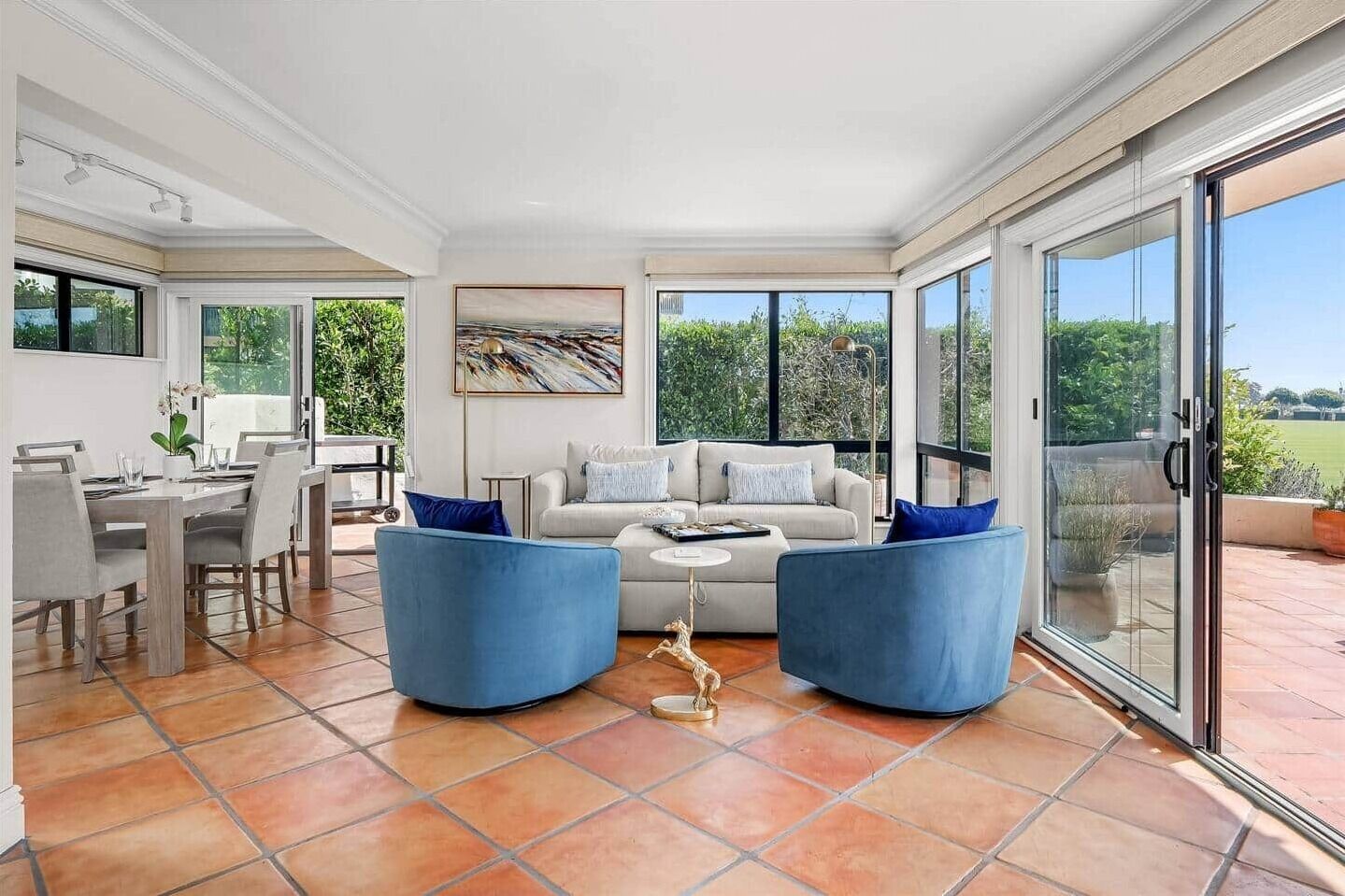 A spacious living room with a large sofa, two blue armchairs, a coffee table, and a dining area with a table and chairs.
